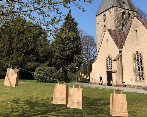 Papiertaschen mit einem Gottesdienst to go Ostern 2020 auf zwei Wäscheleinen vor der Kirche