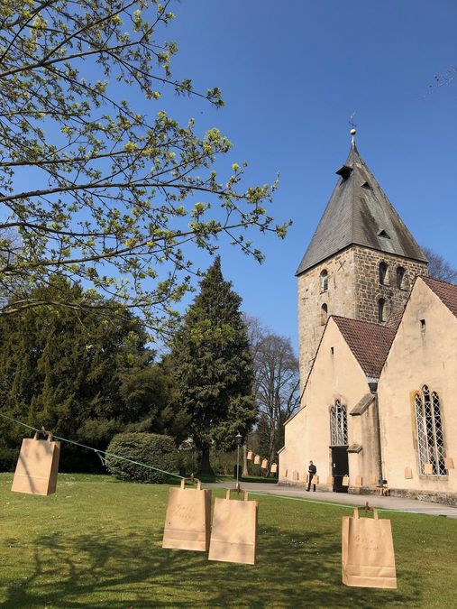 Papiertaschen mit einem Gottesdienst to go Ostern 2020 auf zwei Wäscheleinen vor der Kirche